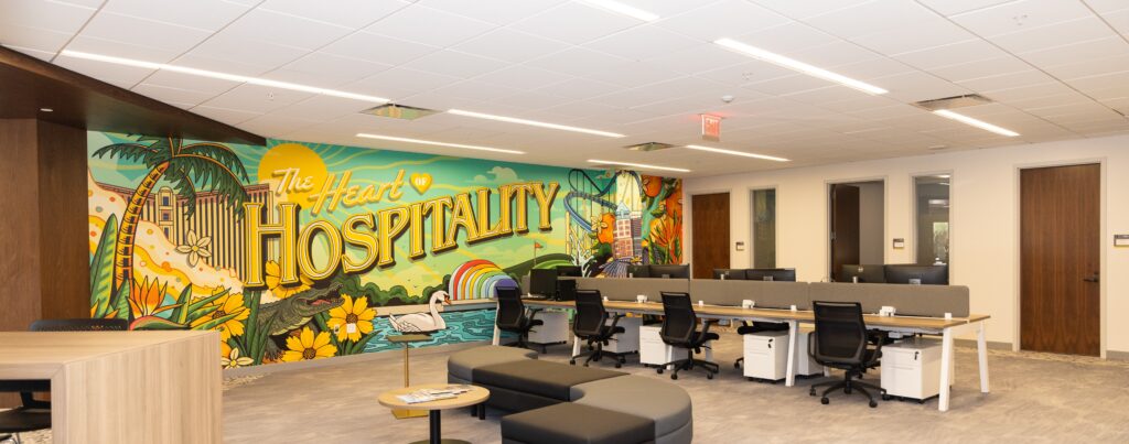 Open office with desks and chairs in front of a colorful mural reading The Heart of Hospitality