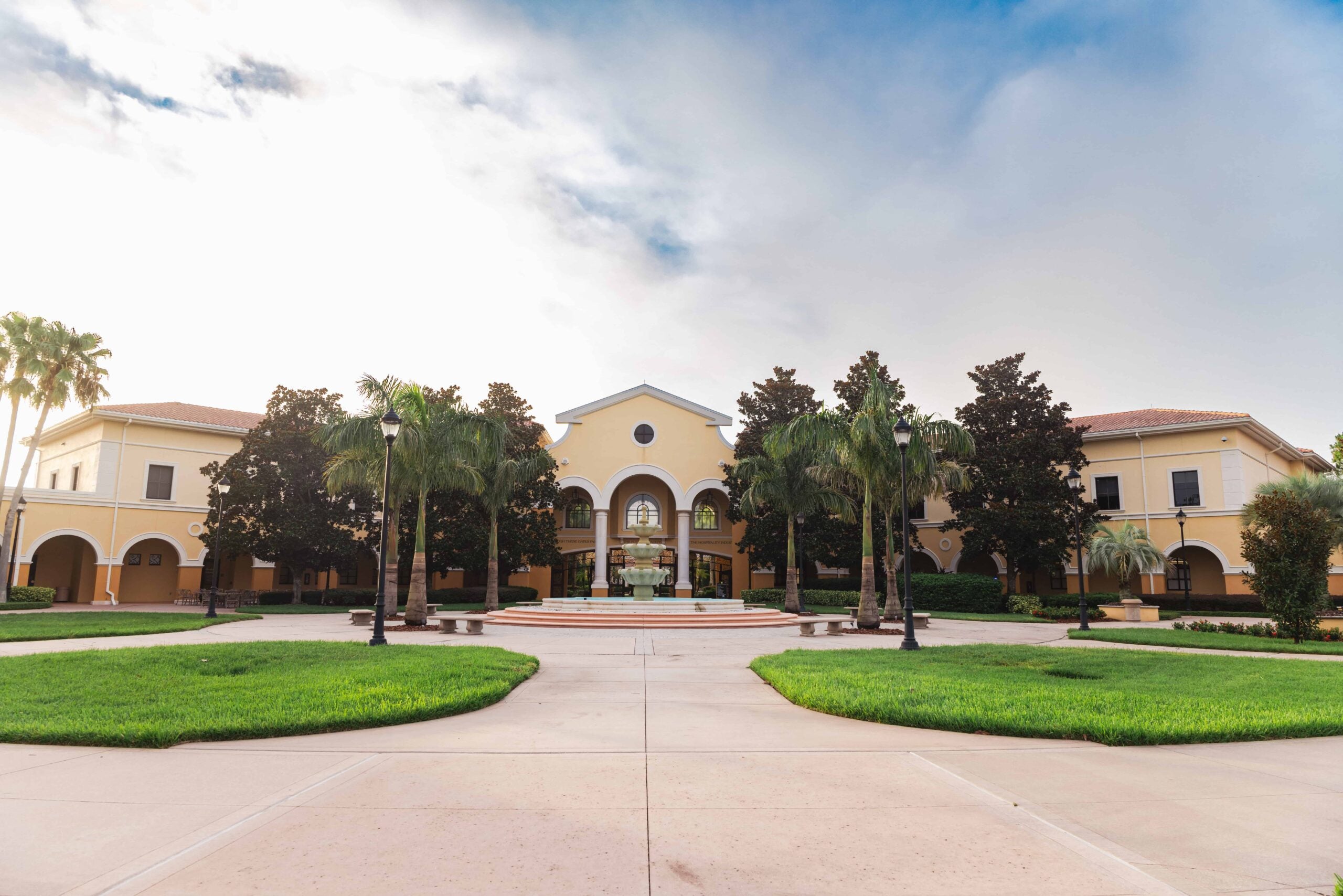 Rosen College courtyard with a fountain, palm trees and the arched main building at dusk