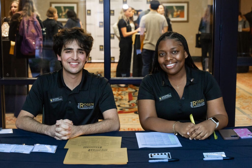 Two student ambassadors in Rosen College Leadership Council polos staffing an event registration table