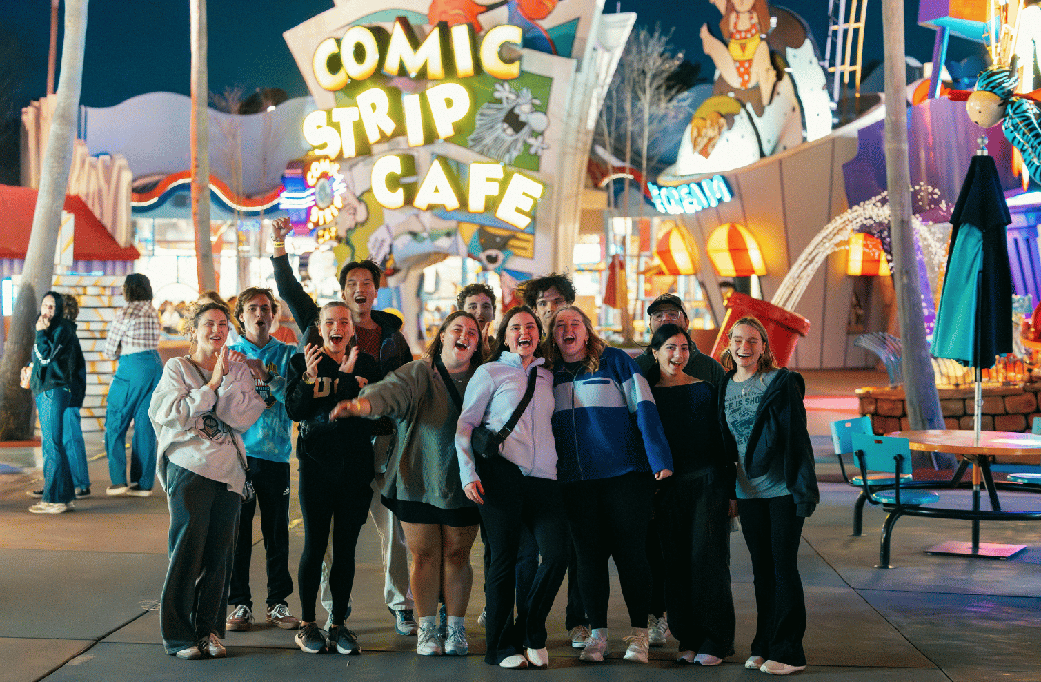 Students cheering outside the Comic Strip Cafe at a theme park at night